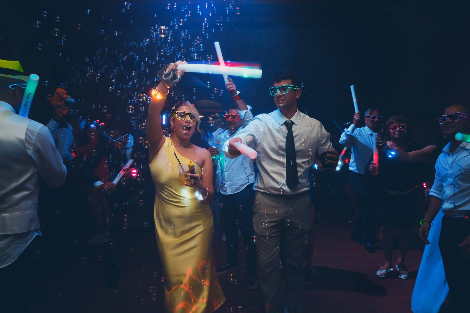 Celebración de boda bajo luces de neón y burbujas, capturada con una estética cinematográfica